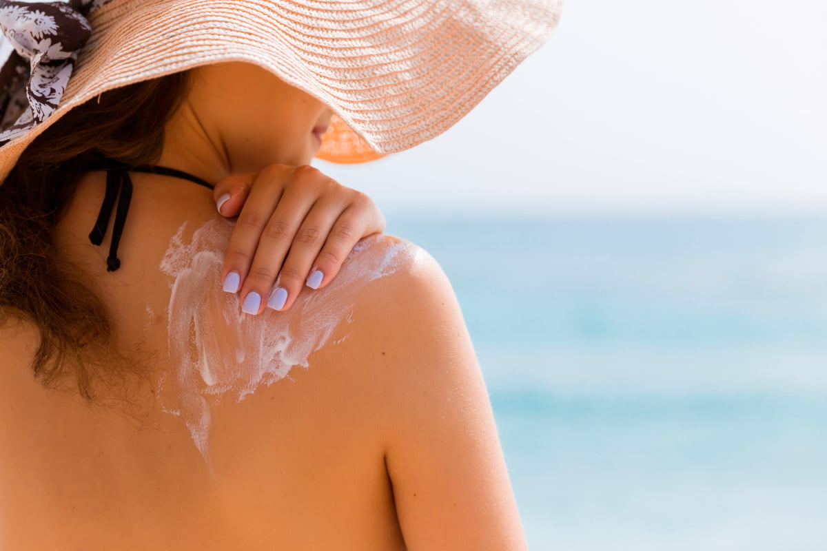 Young woman in straw hat applying sunscreen at the beach in Lafayette