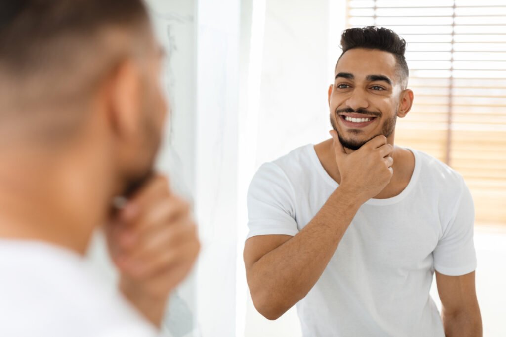 Young man looking in mirror smiling after med spa treatments